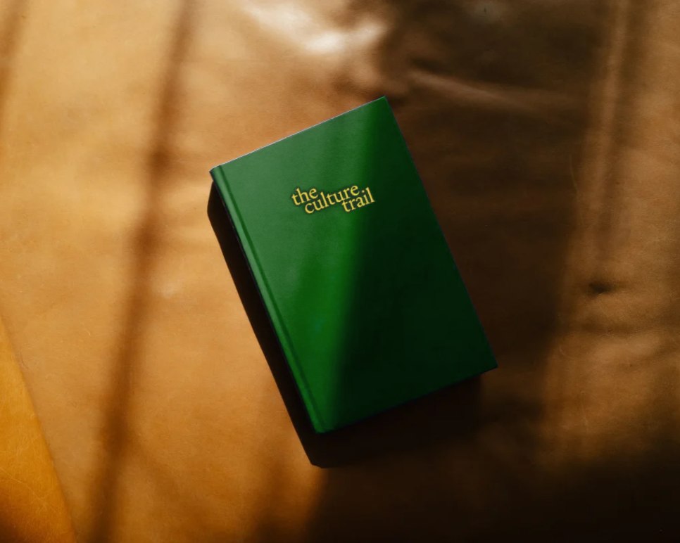 Het merkboek van The Culture Trail, goudfolie op een groen omslag, op een warme ondergrond