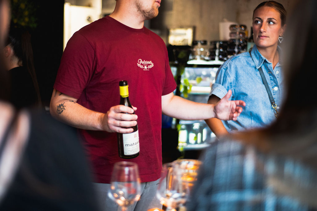 Gastheer met een wijnfles in gesprek met gasten aan de bar